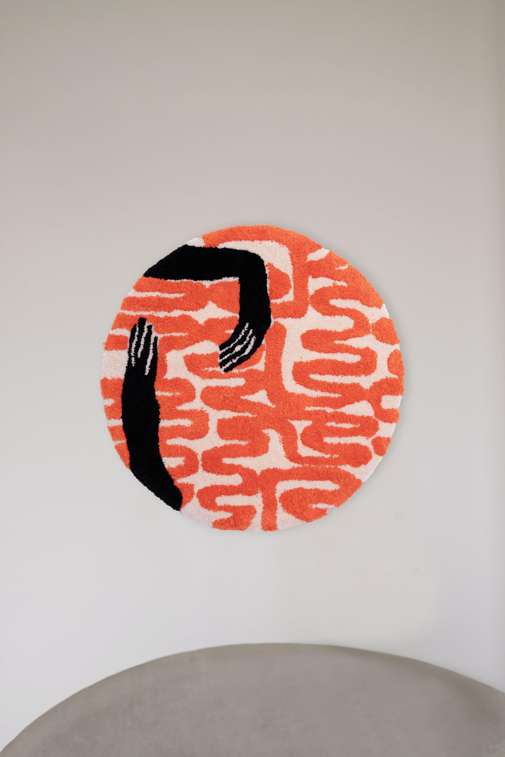 Tufted fabric wall hanging of abstract holding hands in black and orange. Dimensions 750mm x 750mm.